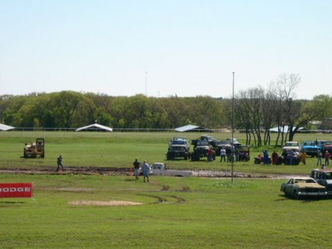 1978 Ford Bronco - A muddy field hosts a gathering of off-road vehicles and spectators under a clear sky.