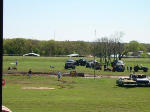 1978 Ford Bronco - A muddy field hosts a vehicle event with multiple trucks and ATVs, some partially submerged in mud.