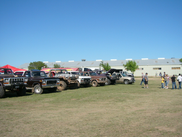 Line of 1978 Ford Broncos and other trucks parked on grass in front of a building