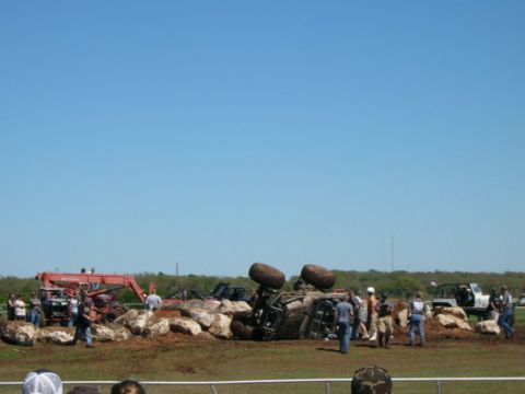 1978 Ford Bronco - An off-road vehicle lies overturned on a pile of rocks, with several people observing the scene.