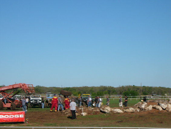 Red Dodge banner in foreground, off-road vehicles and people in muddy field under blue sky