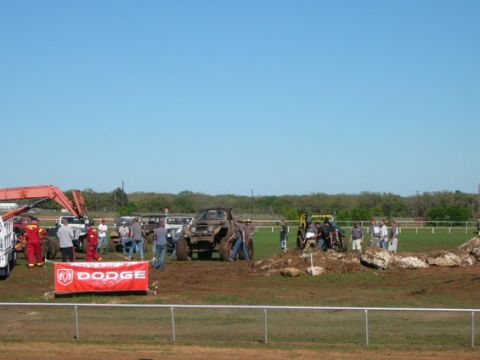 1978 Ford Bronco - A group of people and modified off-road vehicles are gathered in a muddy area under a clear blue sky.