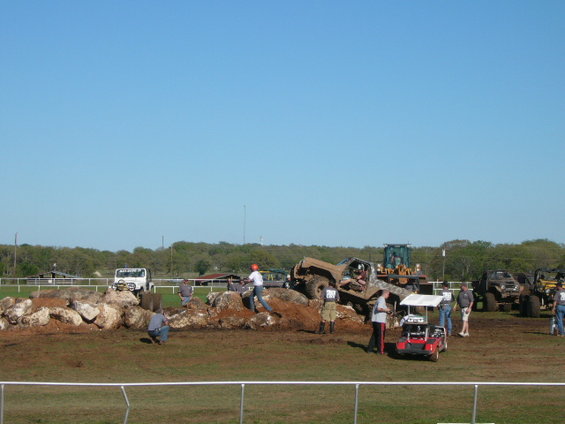 off-road vehicles on a dirt course with rocks and people around