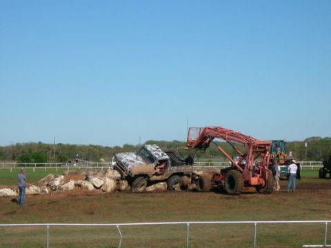 1978 Ford Bronco - An off-road vehicle is stuck on a pile of rocks while a loader attempts to assist.