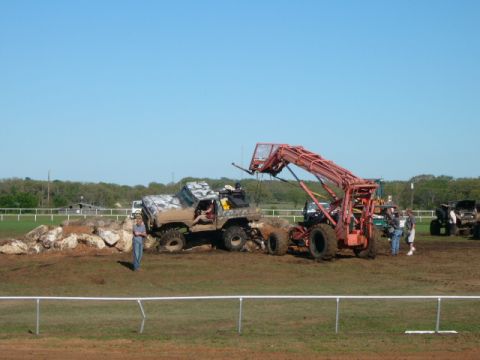 1978 Ford Bronco - An off-road vehicle with camouflage paint is seen maneuvering over rocks, with a large loader and other vehicles present in the background.