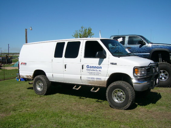 White Ford E-Series van with "Gannon Construction Co., Inc." text and phone number, parked on grass next to a blue pickup truck