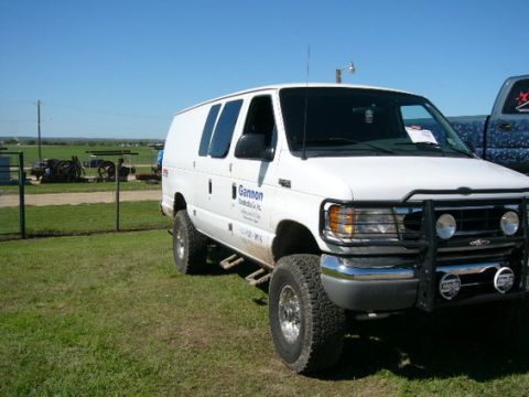 1978 Ford Bronco - Three-quarter front view of a white 4x4 Ford Econoline cargo van parked on grass, fitted with a black brush guard carrying round driving li…