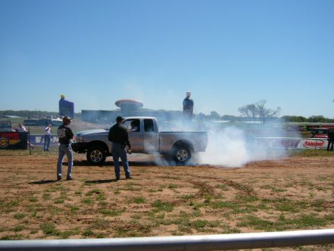 1978 Ford Bronco - A pickup truck is performing a burnout, creating a large cloud of smoke on a sunny day at an outdoor event.