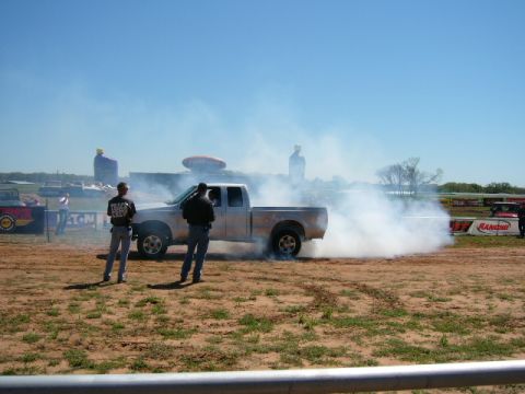 1978 Ford Bronco - A pickup truck performs a burnout, kicking up a large cloud of smoke on a sunny day with spectators and other vehicles present.