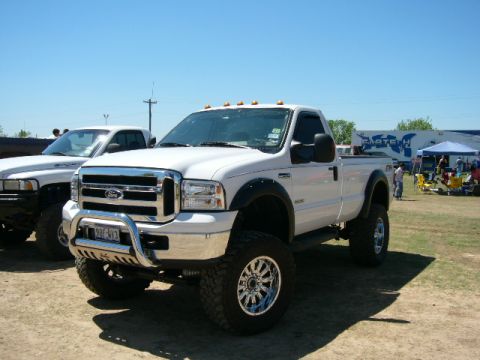 1978 Ford Bronco - White Ford F-250 Super Duty pickup truck with custom wheels and lifted suspension is parked at an outdoor event.