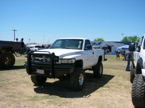 1978 Ford Bronco - White Dodge Ram pickup truck with a bull bar and lifted suspension at an outdoor event.