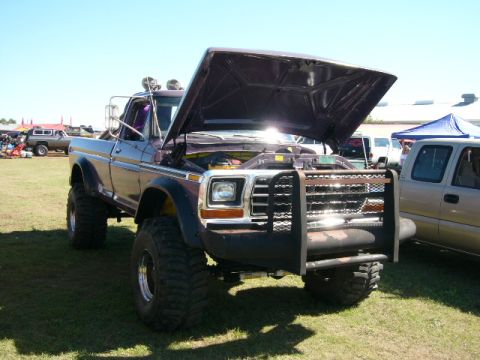 1978 Ford Bronco - Three-quarter front view of a lifted late-1970s Ford F-Series pickup on a grass show field with its hood raised, showing a purple and silve…