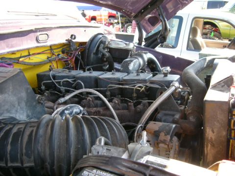 1978 Ford Bronco - Engine bay of a purple vehicle with the hood up, showing an inline diesel engine with a black valve cover, turbocharger and exhaust elbow,…