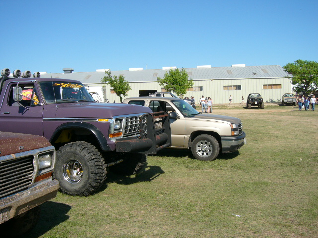 Purple lifted 1970s Ford pickup with roof light bar and mud tires at a grass truck meet