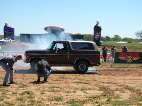 1978 Ford Bronco - A 1978 Ford Bronco performs a burnout at an outdoor event with spectators and large inflatable advertisements in the background.