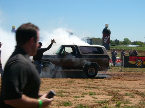 1978 Ford Bronco - A person sprays something from a can while a Ford Bronco performs a burnout, creating a lot of smoke.