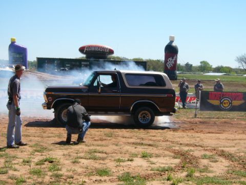 1978 Ford Bronco - A 1978 Ford Bronco performs a burnout at an outdoor event, surrounded by spectators and advertising.