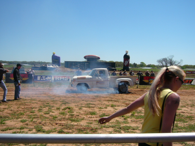 Pickup truck doing a burnout, kicking up smoke. People watching in background