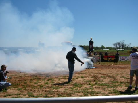 1978 Ford Bronco - A white pickup truck performs a burnout, creating a large cloud of smoke. The scene includes spectators and large inflatable bottles in the…