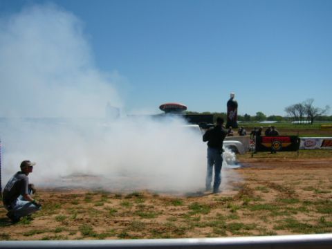 1978 Ford Bronco - A truck performs a burnout at an outdoor event with spectators and advertising banners in the background.