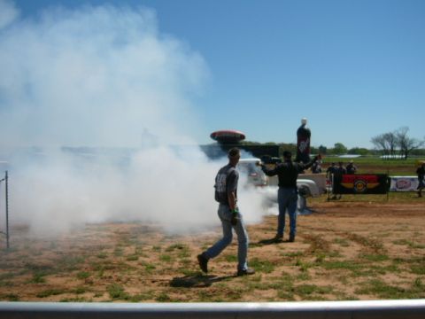 1978 Ford Bronco - A truck is performing a burnout, creating a large cloud of smoke. Two people are standing nearby.