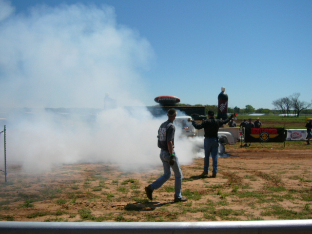 Truck doing a burnout in a dirt lot with two people watching
