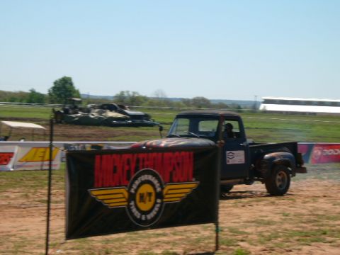1978 Ford Bronco - A vintage pickup truck is seen doing a burnout on a dirt track, with a banner in the foreground.