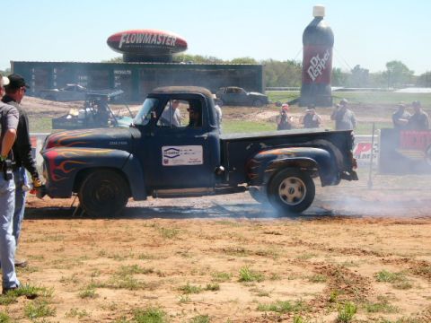 1978 Ford Bronco - A vintage pickup truck performs a burnout at an outdoor event, with large inflatable advertising signs visible in the background.