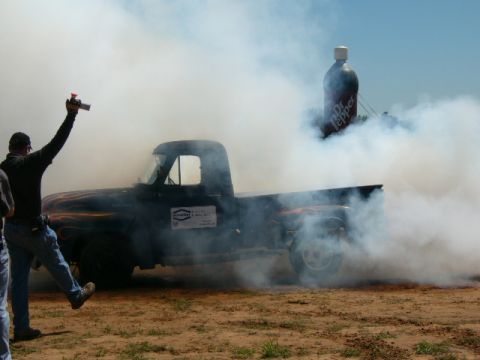 1978 Ford Bronco - A black pickup truck performs a burnout, surrounded by smoke, with a giant Dr. Pepper bottle in the background.