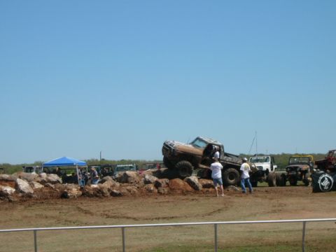1978 Ford Bronco - Several off-road vehicles are gathered at an event, with one truck attempting to climb over rocks.