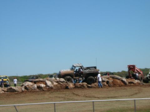 1978 Ford Bronco - A muddy pickup truck navigates a rocky obstacle course with spectators nearby.
