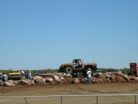 1978 Ford Bronco - An off-road vehicle navigates a rocky obstacle course on a sunny day, with other vehicles and spectators visible.