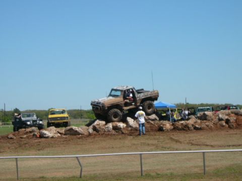 1978 Ford Bronco - A lifted, mud-splattered truck navigates a rocky obstacle course on a sunny day.