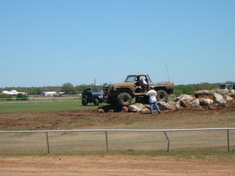 1978 Ford Bronco - Two off-road vehicles are seen on a dirt course with a pile of rocks.