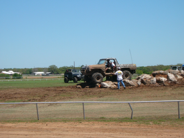 Muddy off-road truck with big tires navigating rocks, another SUV nearby