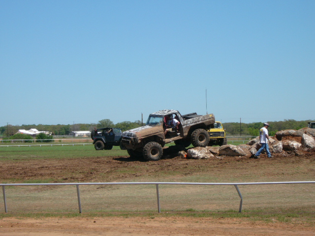 Mud-splattered 1978 Ford Bronco climbing over rocks, with a blue Jeep and yellow truck behind it