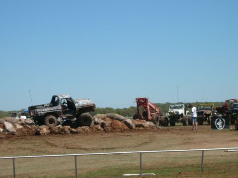 1978 Ford Bronco - Several off-road vehicles are gathered on a dirt course with a clear blue sky overhead.