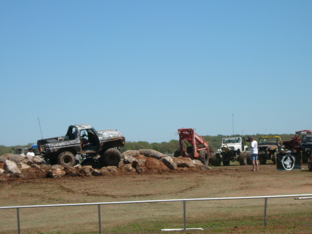 Modified 1978 Ford Bronco climbing over rocks, with other off-road vehicles and people in the background