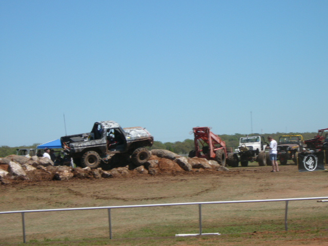muddy off-road vehicles on rocky terrain, some jeeps and a truck in background