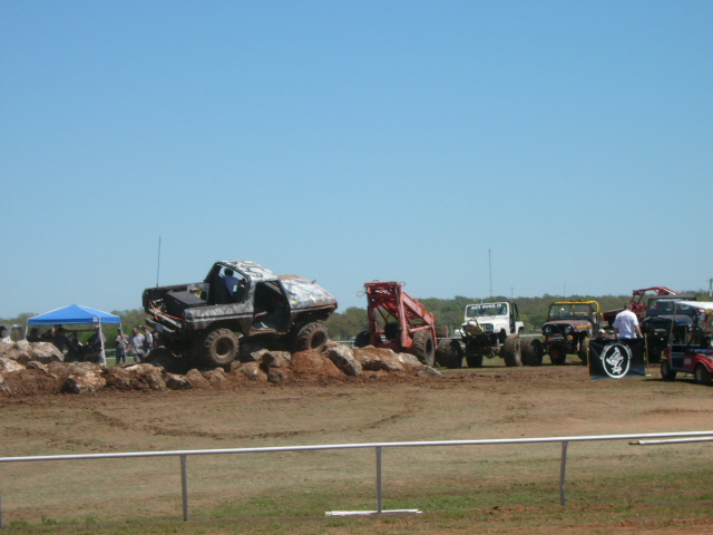 Off-road vehicles on a dirt course with a blue tent and spectators