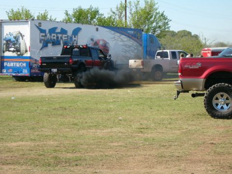 1978 Ford Bronco - Pickup truck emits thick black smoke while driving in a grassy field with other vehicles present.
