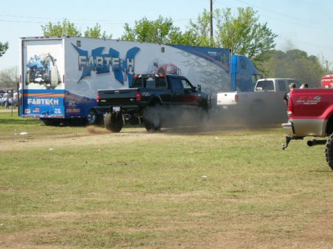 1978 Ford Bronco - A black Ford pickup truck kicks up a lot of smoke while performing a burnout in front of a large trailer.