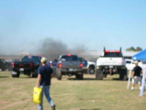 1978 Ford Bronco - Multiple pickup trucks are shown, with one emitting a large cloud of black smoke under a clear blue sky.