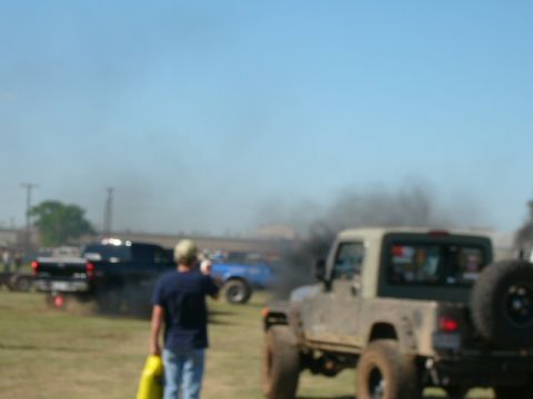 1978 Ford Bronco - Several trucks are seen emitting large amounts of black smoke in an outdoor, grassy area under a clear blue sky.
