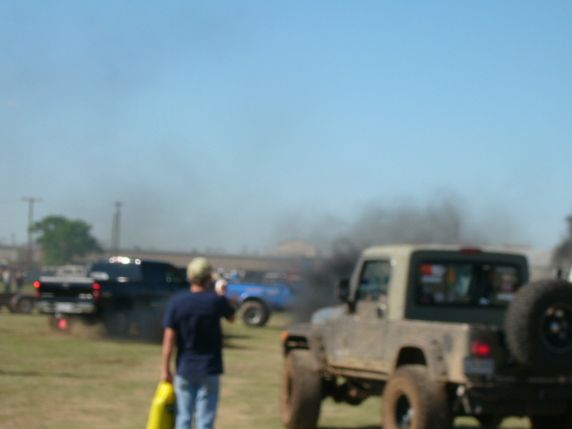 Guy with yellow jug watches trucks spew black smoke