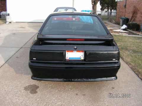 1988 Ford Mustang - The rear of a black 1988 Ford Mustang hatchback is shown parked on a concrete driveway.