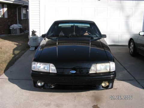 1988 Ford Mustang - A black 1988 Ford Mustang is parked in a driveway in front of a garage door, with another car to its right.