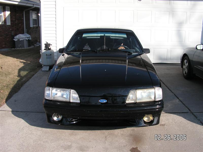Black 1988 Ford Mustang parked in front of a garage. Another car is visible to the right