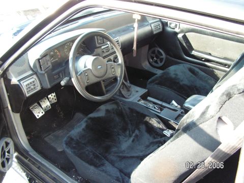 1988 Ford Mustang - Interior view of a car with fuzzy seat covers and aftermarket pedals.