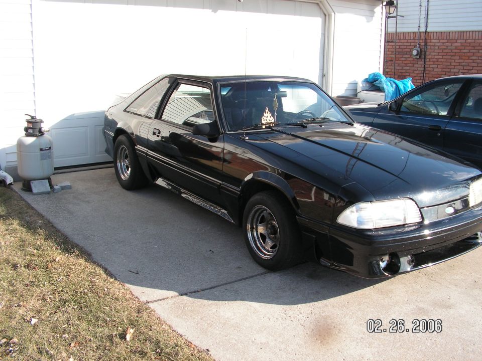 Black coupe parked in front of a garage, another car is parked to the right
